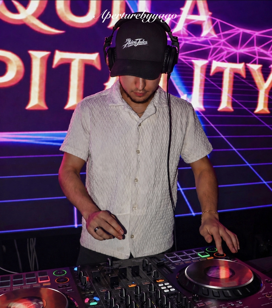 DJ Aiden Jules mixing on club CDJs in a branded cap against a neon laser-grid backdrop