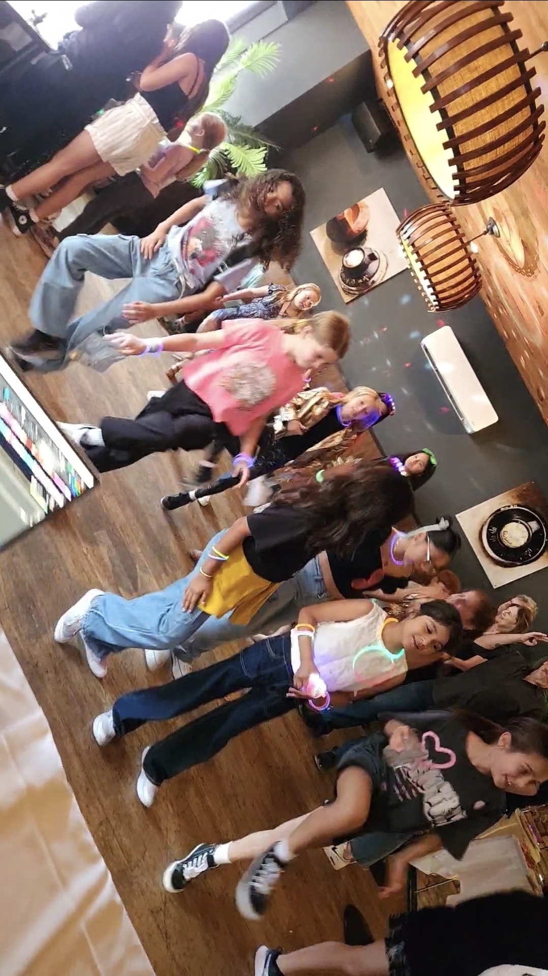 Guests wearing glow sticks and bracelets dancing on a hardwood floor at a birthday celebration