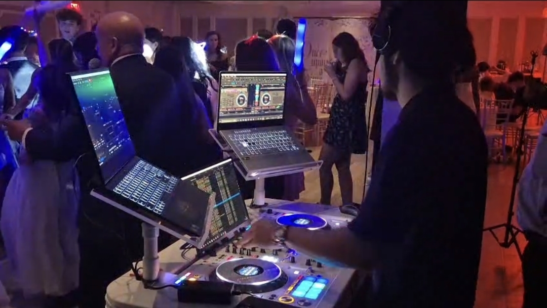 DJ Aiden Jules performing on dual laptops and controller as guests dance at a Quinceañera reception