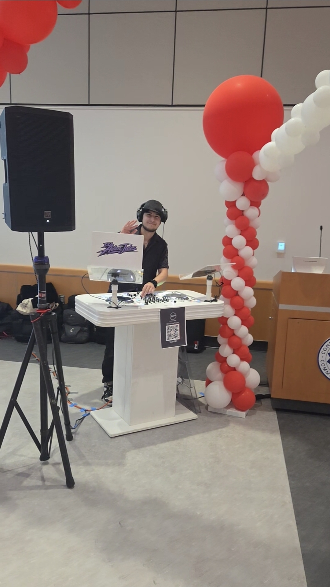 DJ Aiden Jules waving from a white DJ booth with red and white balloon column