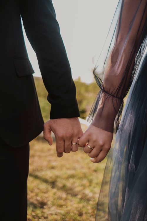 Couple in wedding attire holding hands with rings visible in warm outdoor light