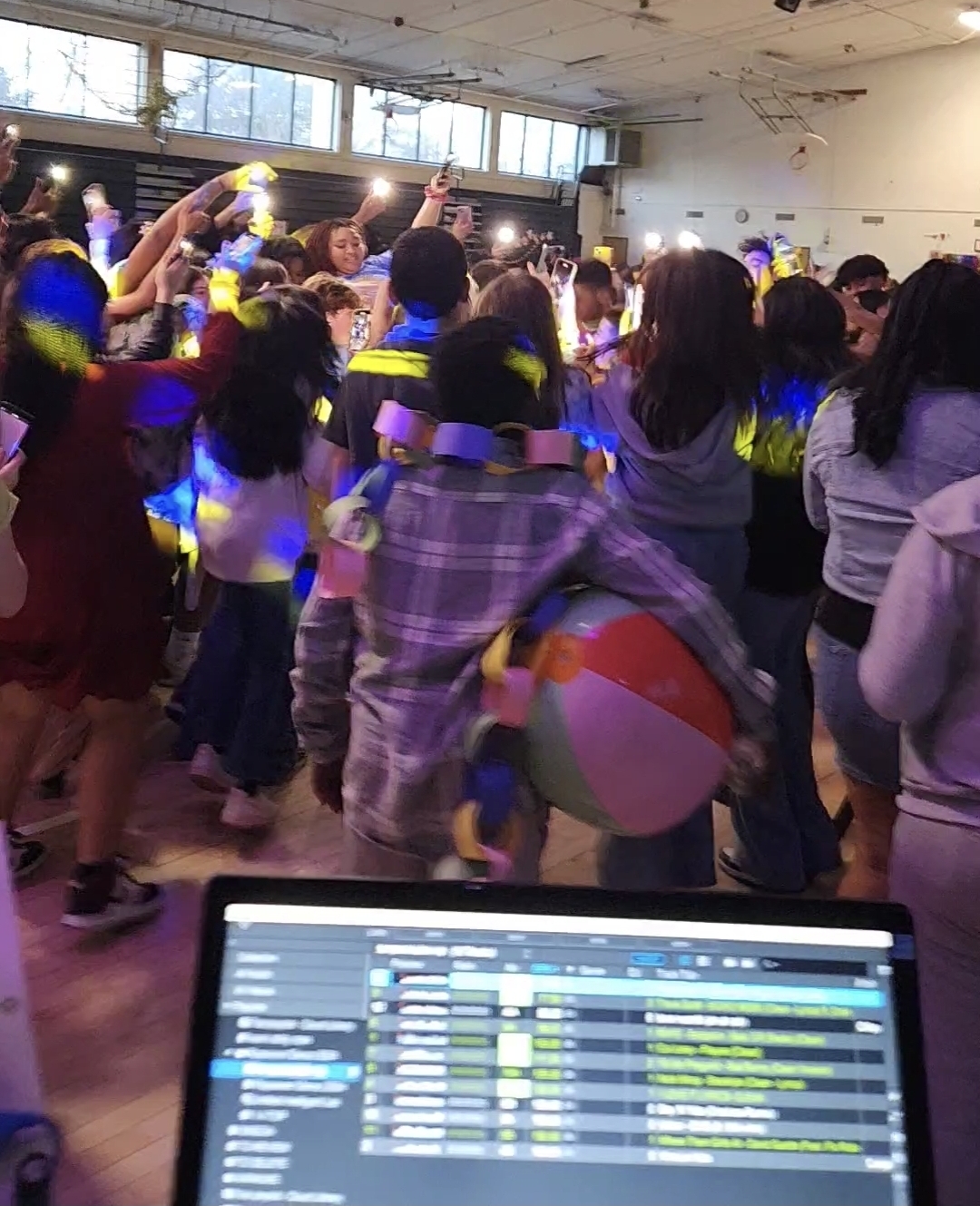 School dance crowd with phone flashlights raised and glow accessories during a high-energy moment